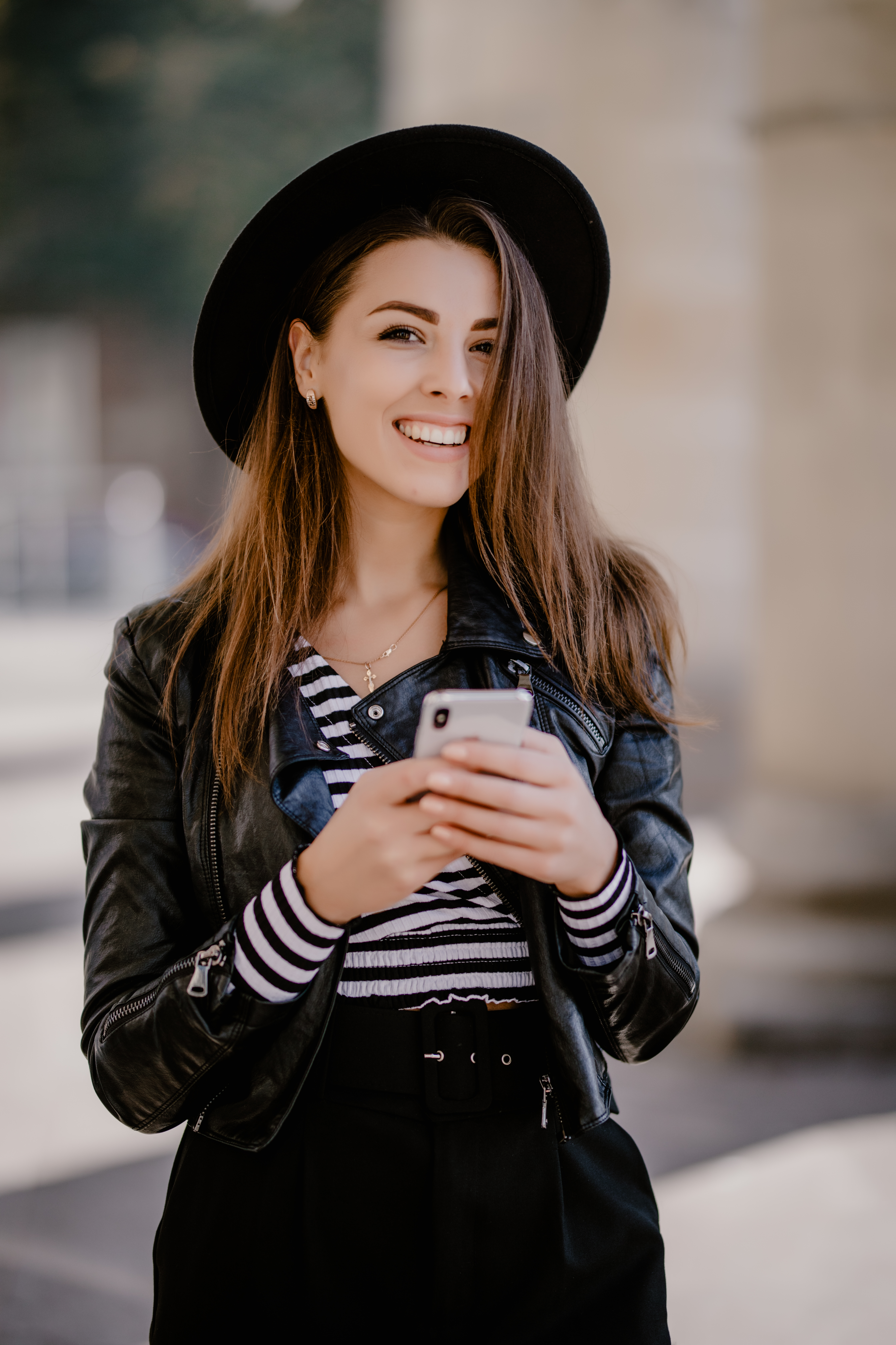 young-brown-haired-girl-leather-jacket-black-hat-city-promenade-posing-with-mobile-phone